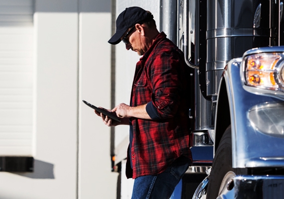 Man on tablet next to his commercial trucking vehicle